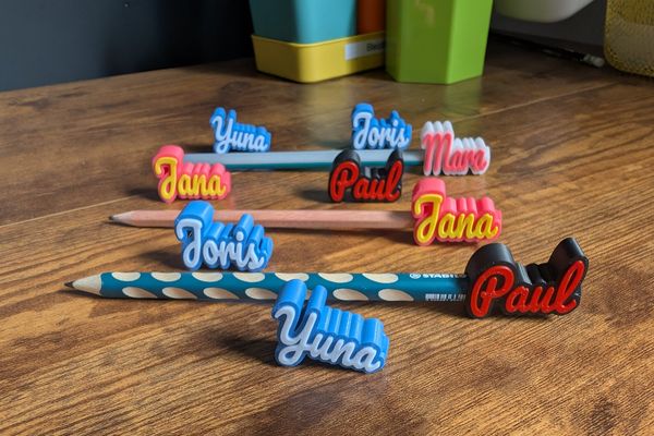 Personalisierte Stiftaufsätze mit den Namen 'Paul', 'Yuna' und 'Mara' auf Buntstiften
